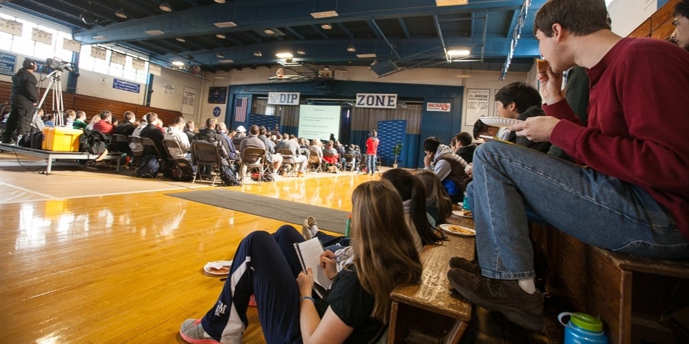 Franklin & Marshall case study: photograph of students at the university's "Common Hour," seated in a gymnasium, listening and taking notes.