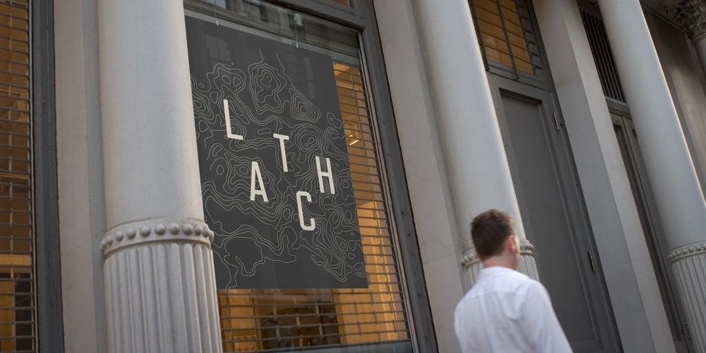 LATCH case study: the letters of LATCH in white against a dark grey banner with darker contour lines, as with a topographic map. The banner is shown hanging between the columns of a city building.